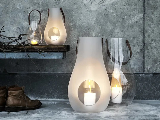Et fremragende eksempel på stilfulde og smukke gaver til kvinder: Design med lys-lanterne fra Holmegaard lavet af gennemsigtigt eller matt hvidt glas og et læderhåndtag.