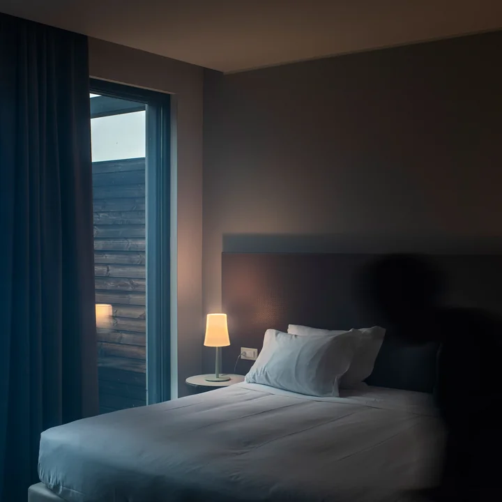 Birdie Easy bordlampe fra Foscarini på sengebordet ved siden af en seng ved vinduet